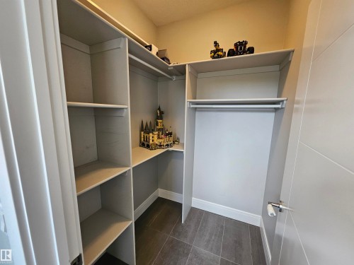 Walk-in closet featuring built-in shelving, a dedicated hanging rod, dark grey tile flooring, and light grey painted walls - 9311 66 Avenue Nw, Edmonton, AB - Indoor With Storage