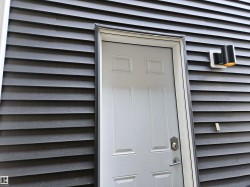 White paneled door with a brushed metal handle, set against dark horizontal siding - 