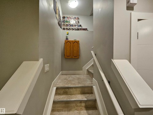 Stairway featuring a wall-mounted light fixture, light gray wall paint, white trim, and a wood-finish wall cabinet - 9311 66 Avenue Nw, Edmonton, AB - Indoor Photo Showing Other Room