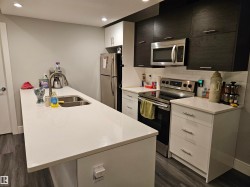 Modern kitchen featuring white countertops, stainless steel appliances, dark wood-finish upper cabinetry, white lower cabinetry, and wood-finish flooring - 