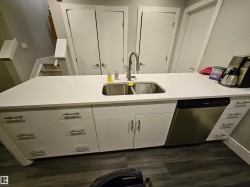 Contemporary kitchen island featuring a white countertop with an undermount double-basin stainless steel sink and a pull-down faucet - 