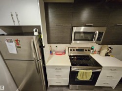 Contemporary kitchen featuring white shaker-style cabinetry, wood-finish upper cabinetry, stainless steel appliances, white countertops, and a white subway tile backsplash - 