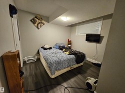 Room featuring wood-finish flooring, a wall-mounted television, and a window with blinds - 