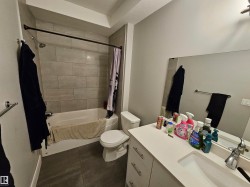 Full bathroom featuring a white tub, light gray subway-tiled shower surround, dark gray large-format floor tiles, a white vanity with an integrated sink, and a large wall-mounted mirror - 