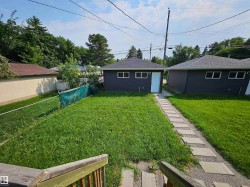 Expansive grassy yard area with a paver walkway leading to a detached structure featuring dark siding, a light-colored door, and multiple windows - 