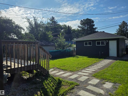 Expansive grassy yard with a wooden deck, stepping stone pathway, and a detached structure with dark siding and a white entry door - 9311 66 Avenue Nw, Edmonton, AB - Outdoor