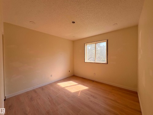 Spacious room featuring wood-finish flooring, neutral-toned walls, a large window, and recessed lighting - 18007 73 Avenue Nw, Edmonton, AB - Indoor Photo Showing Other Room