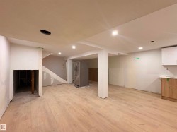 Spacious open-concept area featuring wood-finish flooring, recessed lighting, and a partially installed kitchen with light wood cabinetry and white upper cabinets - 
