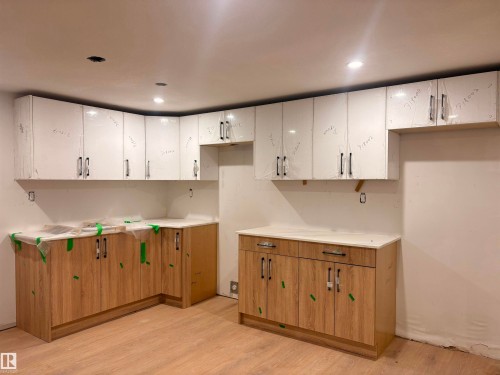 Kitchen featuring white marble-finish cabinetry with brushed metal hardware, wood-finish base cabinetry, quartz countertops, recessed lighting, and wood-finish flooring throughout - 18007 73 Avenue Nw, Edmonton, AB - Indoor