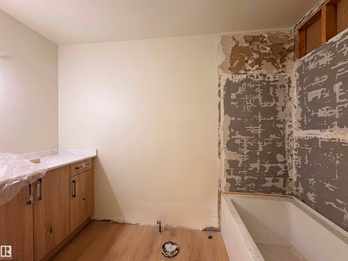Wood-finish flooring, white bathtub, wood vanity cabinetry with dark hardware, and light-toned countertop - 18007 73 Avenue Nw, Edmonton, AB - Indoor Photo Showing Bathroom