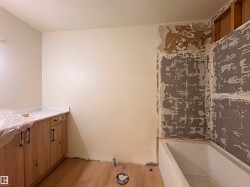 Wood-finish flooring, white bathtub, wood vanity cabinetry with dark hardware, and light-toned countertop - 