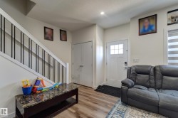 Foyer featuring a white entry door with glass panes, wood-finish flooring, and a staircase with white risers and black metal balusters - 