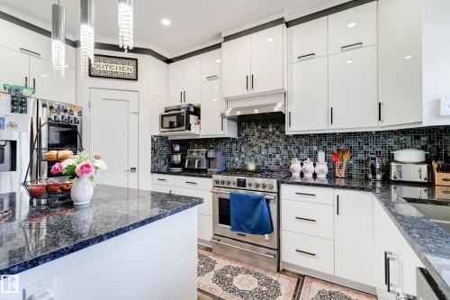 Kitchen featuring white high-gloss cabinetry, dark stone countertops, mosaic tile backsplash, and stainless steel appliances - #8 1703 16 Av Nw Nw, Edmonton, AB - Indoor Photo Showing Kitchen With Upgraded Kitchen