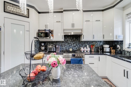 Kitchen featuring an island with a speckled countertop, white cabinetry, dark mosaic tile backsplash, stainless steel range with overhead vent, and pendant light fixtures - #8 1703 16 Av Nw Nw, Edmonton, AB - Indoor Photo Showing Kitchen With Upgraded Kitchen