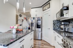 Contemporary kitchen featuring white cabinetry, dark stone countertops, stainless steel appliances, and a mosaic tile backsplash - 