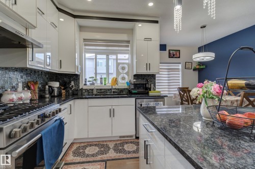 Kitchen featuring white high-gloss cabinetry, black granite countertops, a mosaic tile backsplash, and stainless steel appliances - #8 1703 16 Av Nw Nw, Edmonton, AB - Indoor Photo Showing Kitchen With Upgraded Kitchen