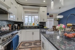 Kitchen featuring white high-gloss cabinetry, black granite countertops, a mosaic tile backsplash, and stainless steel appliances - 