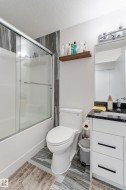 Bathroom featuring a shower-tub combination with sliding glass doors, a white toilet, and a vanity with a dark countertop and white cabinetry - 