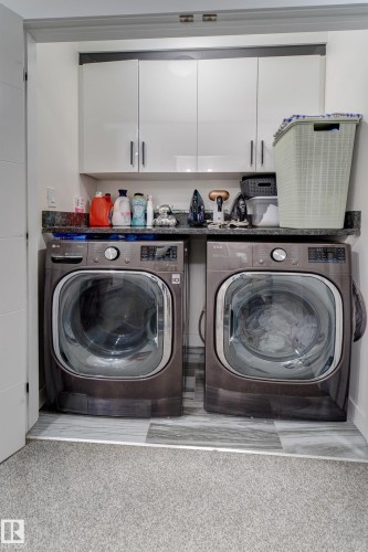 Dedicated laundry area featuring front-loading machines, granite-style countertop, and white upper cabinetry - #8 1703 16 Av Nw Nw, Edmonton, AB - Indoor Photo Showing Laundry Room