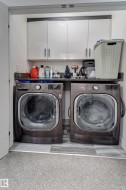 Dedicated laundry area featuring front-loading machines, granite-style countertop, and white upper cabinetry - 