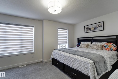 Bedroom featuring two windows with horizontal blinds, overhead drum light fixture, and grey carpeting - #8 1703 16 Av Nw Nw, Edmonton, AB - Indoor Photo Showing Bedroom