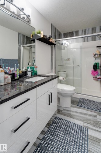 Vanity featuring a dark stone-finish countertop with an undermount sink, sleek white cabinetry with black and chrome hardware, and a large wall-mounted mirror - #8 1703 16 Av Nw Nw, Edmonton, AB - Indoor Photo Showing Bathroom