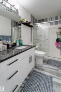 Vanity featuring a dark stone-finish countertop with an undermount sink, sleek white cabinetry with black and chrome hardware, and a large wall-mounted mirror - 