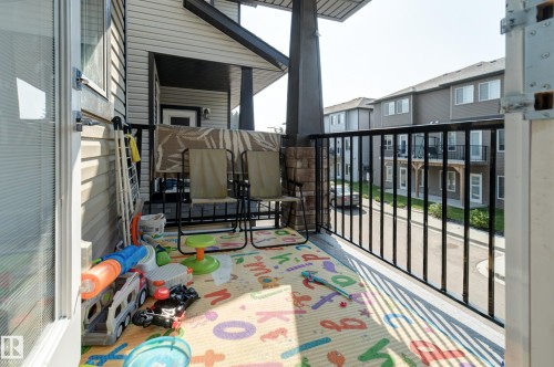 Spacious balcony featuring durable vinyl siding, a black metal railing, and a stone-clad column base - #8 1703 16 Av Nw Nw, Edmonton, AB - 