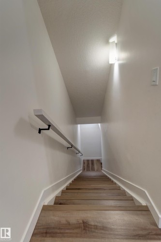 Staircase featuring wood-finish treads, a contrasting handrail with black brackets, and recessed wall lighting - #8 1703 16 Av Nw Nw, Edmonton, AB - Indoor Photo Showing Other Room