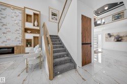 Double-height entryway featuring a modern staircase with glass railing and wood-finish handrail, alongside white and gold veined porcelain tile flooring - 