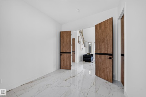 Entryway featuring large format white tile flooring with veining, solid wood-finish doors with black banding and hardware, and bright white walls - 112 Ross Close, Leduc, AB - Indoor