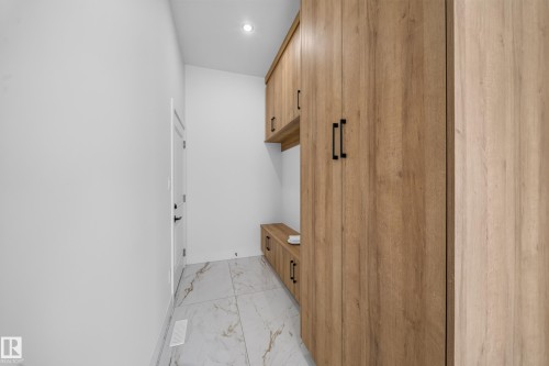 Entryway mudroom with light wood-finish cabinetry, built-in bench, and white large-format tile flooring - 112 Ross Close, Leduc, AB - Indoor Photo Showing Other Room