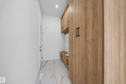 Entryway mudroom with light wood-finish cabinetry, built-in bench, and white large-format tile flooring - 
