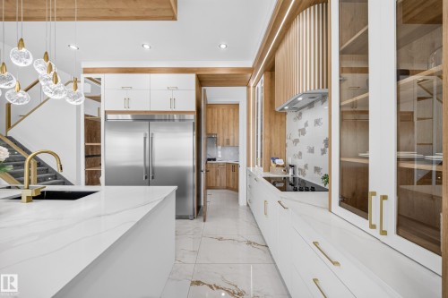 Contemporary kitchen featuring white cabinetry with brass hardware, a large island with a black undermount sink and brass faucet, and integrated stainless steel appliances - 112 Ross Close, Leduc, AB - Indoor Photo Showing Kitchen With Upgraded Kitchen