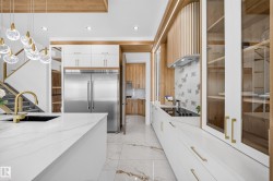 Contemporary kitchen featuring white cabinetry with brass hardware, a large island with a black undermount sink and brass faucet, and integrated stainless steel appliances - 
