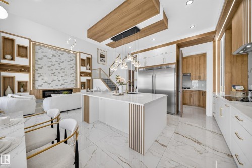 Open-concept living space featuring a central kitchen island with a quartz countertop, integrated stainless steel appliances, marble-look tile flooring, and custom wood-paneled walls - 112 Ross Close, Leduc, AB - Indoor Photo Showing Kitchen
