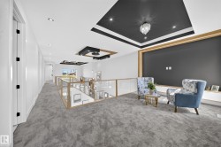 Open-concept upper-level landing featuring a wood-frame and glass railing, recessed lighting, and a custom ceiling design with a contemporary chandelier - 