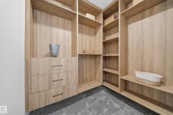 Custom closet system featuring light wood-finish cabinetry, integrated shelving, three drawers with dark hardware, and gray carpet flooring - 