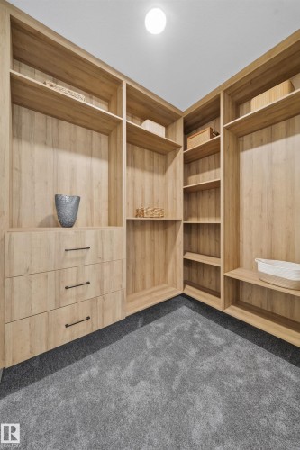 Custom closet system featuring light wood-finish cabinetry, integrated shelving, three drawers with dark hardware, and grey carpet flooring - 112 Ross Close, Leduc, AB - Indoor Photo Showing Other Room