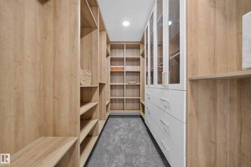 Custom closet system featuring light wood-finish shelving, built-in white cabinetry with glass doors, gold-finish hardware, and soft gray carpeting - 112 Ross Close, Leduc, AB - Indoor