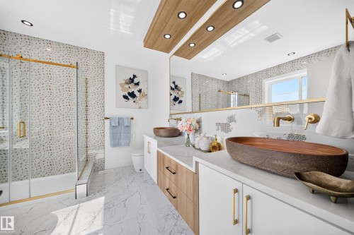 Modern bathroom featuring a dual vanity with unique vessel sinks, a spacious shower with gold-accented glass enclosure, and contemporary wall-mounted faucets - 112 Ross Close, Leduc, AB - Indoor
