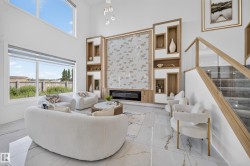 Living area featuring a floor-to-ceiling accent wall with integrated shelving and an electric fireplace, soaring ceilings, large format tile flooring, expansive windows, and a staircase with glass railing - 