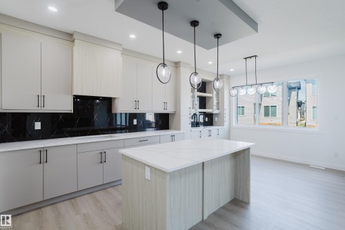 Contemporary kitchen featuring a large central island, light wood-finish flooring, and ample cabinetry - 8728 182 Avenue Nw, Edmonton, AB - Indoor Photo Showing Kitchen With Upgraded Kitchen