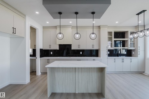 Open-concept kitchen featuring an island with a white countertop, light-toned cabinetry, dark marble-look backsplash, wood-finish flooring, and contemporary pendant lighting - 8728 182 Avenue Nw, Edmonton, AB - Indoor Photo Showing Kitchen With Upgraded Kitchen
