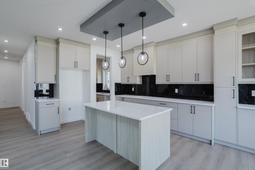 Contemporary kitchen featuring light wood-finish flooring, a central island with a white countertop, light-toned cabinetry, a dark backsplash, and recessed lighting - 8728 182 Avenue Nw, Edmonton, AB - Indoor Photo Showing Kitchen