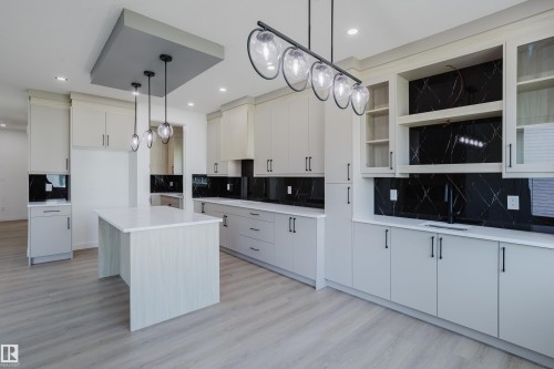Spacious kitchen featuring light wood-finish flooring, white cabinetry with black hardware, white countertops, and black patterned backsplash - 8728 182 Avenue Nw, Edmonton, AB - Indoor Photo Showing Kitchen