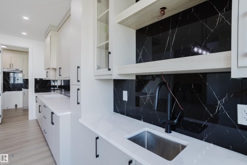 Contemporary kitchen featuring white cabinetry, black marble-look backsplash, light wood-finish flooring, and recessed lighting - 8728 182 Avenue Nw, Edmonton, AB - Indoor Photo Showing Kitchen