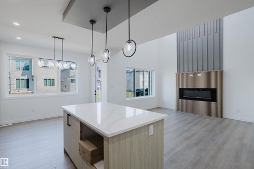 Open-concept living space featuring a contemporary electric fireplace with wood slat detailing, vaulted ceilings, and light wood-finish flooring - 8728 182 Avenue Nw, Edmonton, AB - Indoor With Fireplace