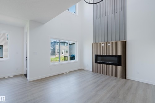 Living area featuring a floor-to-ceiling fireplace with wood slat detailing and an integrated electric firebox, an expansive window, a secondary window, and wood-finish flooring - 8728 182 Avenue Nw, Edmonton, AB - Indoor Photo Showing Living Room With Fireplace