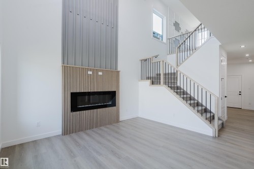 Two-story living area featuring a built-in linear fireplace with wood slat surround, wood-finish flooring, a contemporary staircase with metal balusters, and recessed lighting - 8728 182 Avenue Nw, Edmonton, AB - Indoor With Fireplace